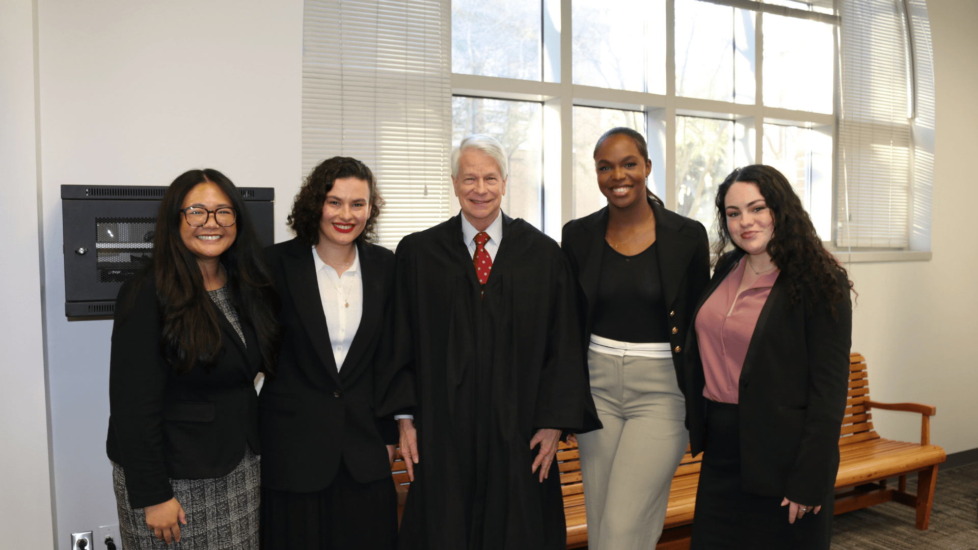 Judge in robe with four smiling women in business attire, indoors.