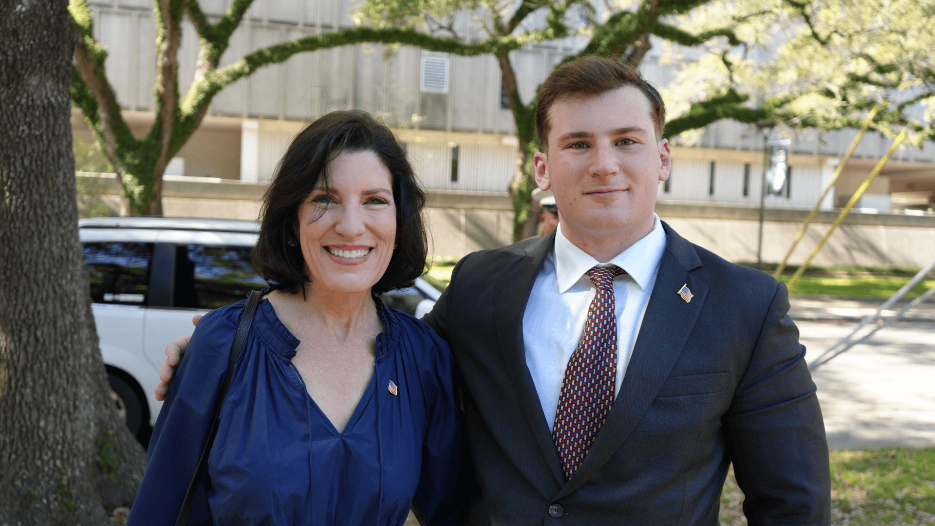 Smiling woman in blue top standing next to a man in a suit outdoors.