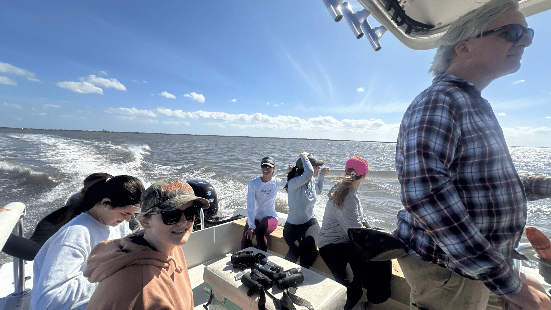 People on a boat, moving across water under a sunny blue sky.