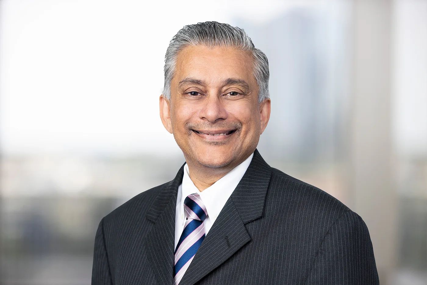 Professional headshot of a smiling man with grey hair wearing a pinstripe suit and striped tie.