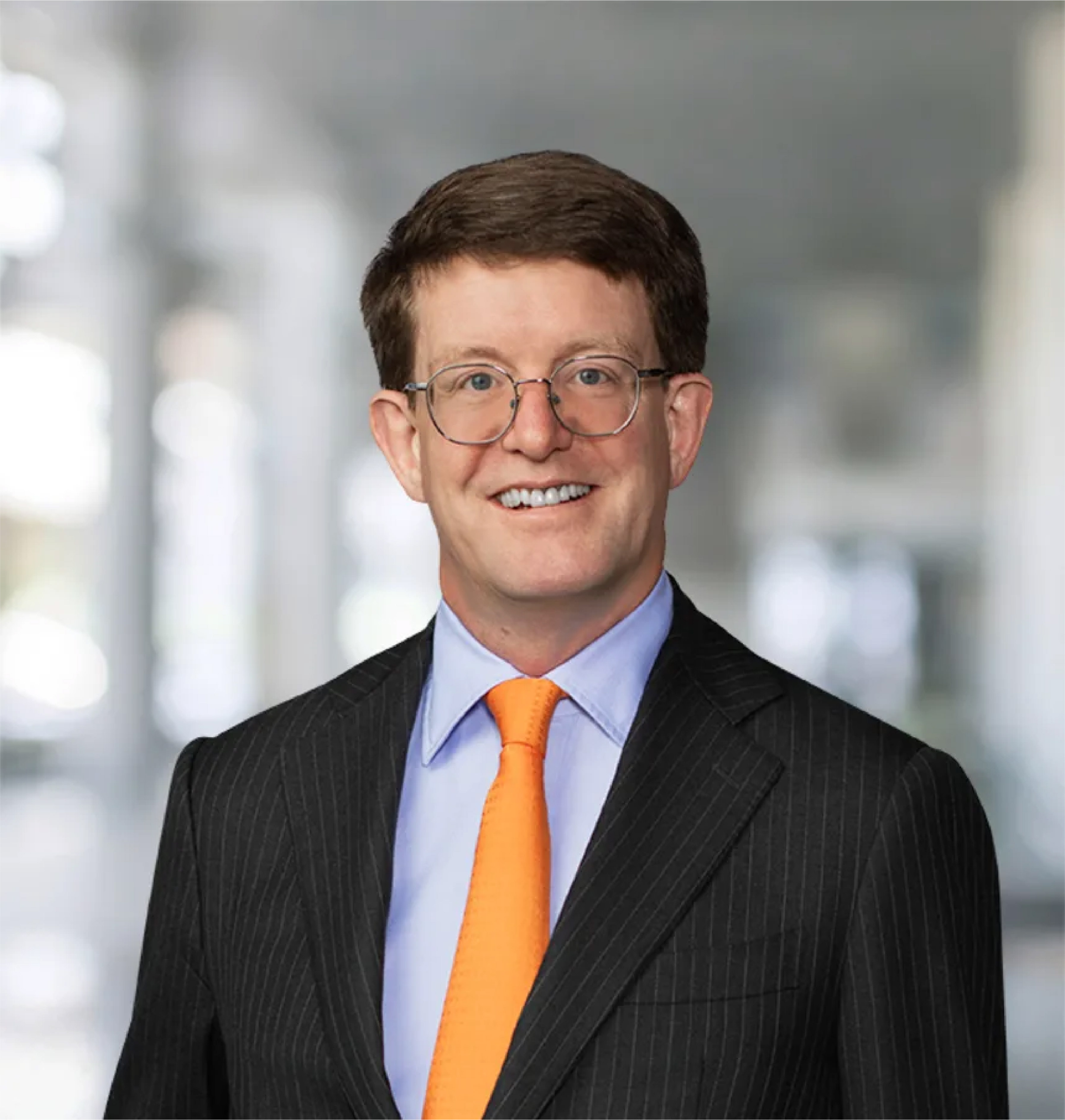 Smiling man in dark pinstripe suit, blue shirt, and orange tie.