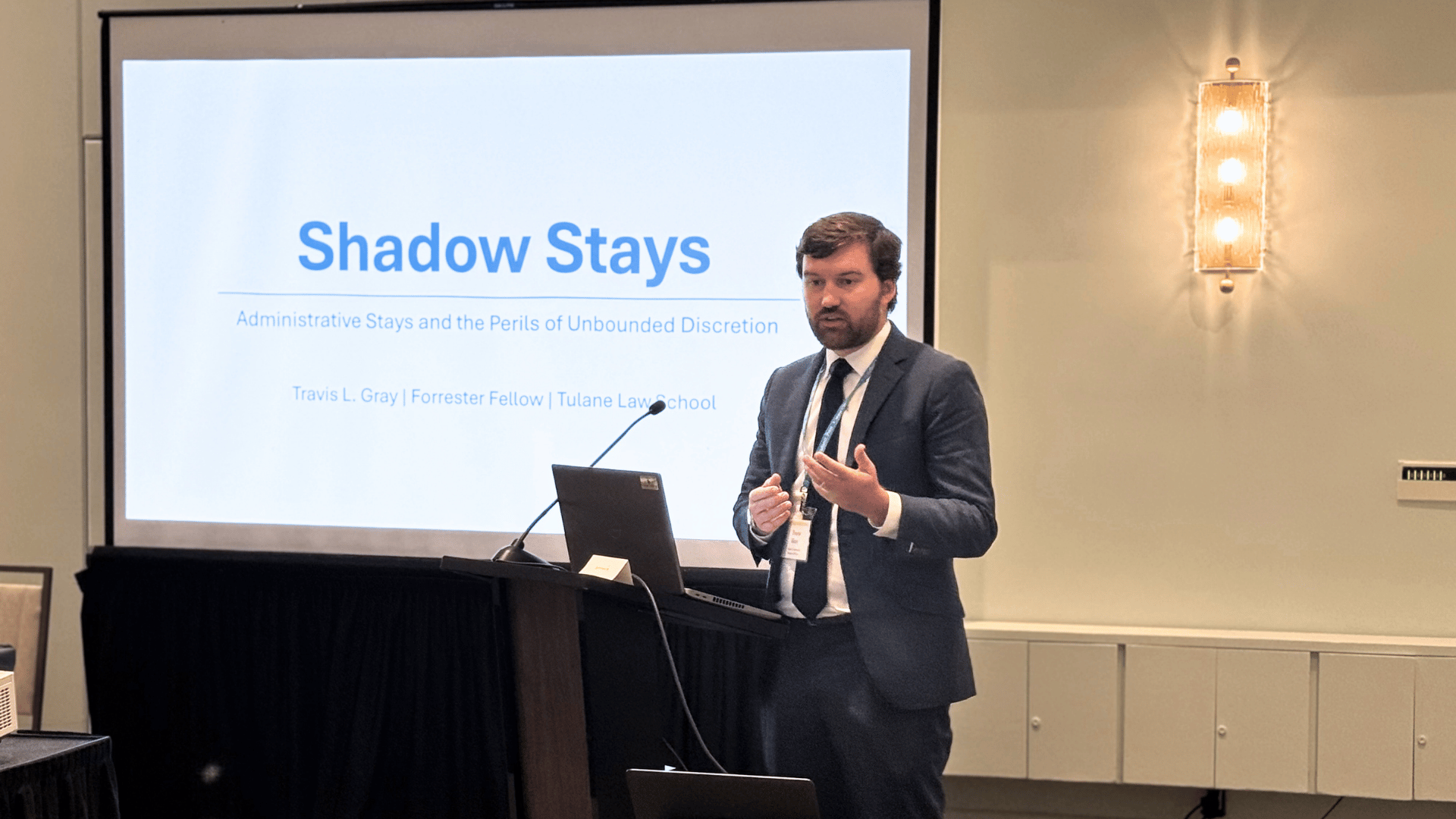 Photograph: Man in suit presents "Shadow Stays" on a large screen.