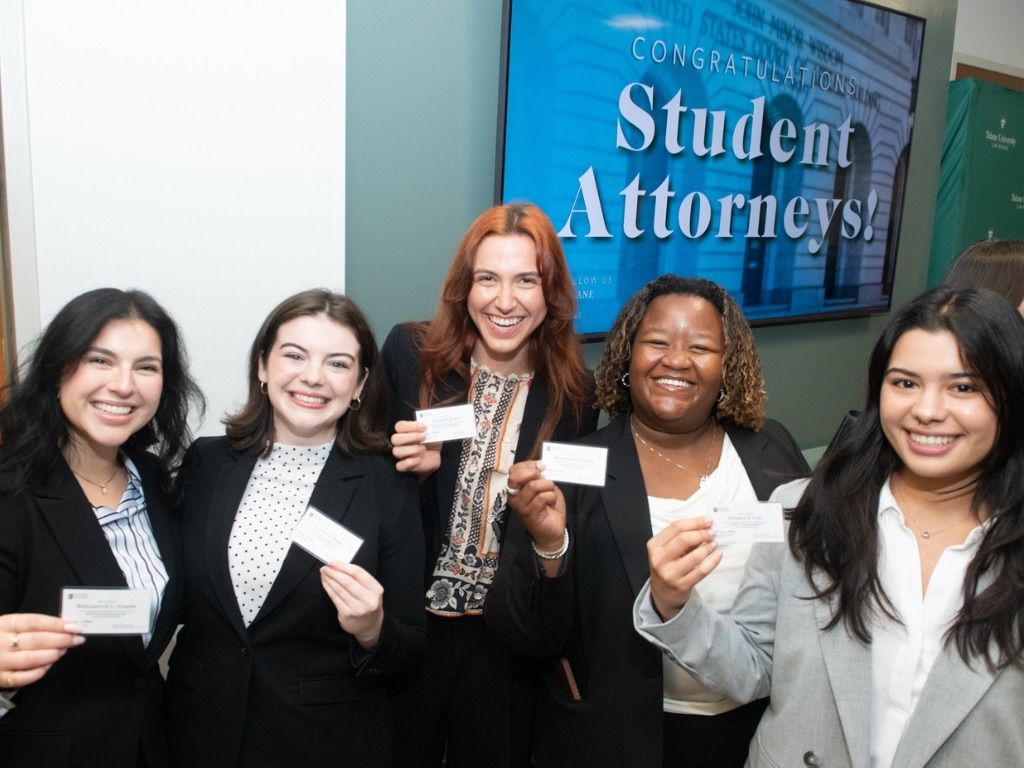 Five smiling student attorneys in blazers proudly hold up small white cards