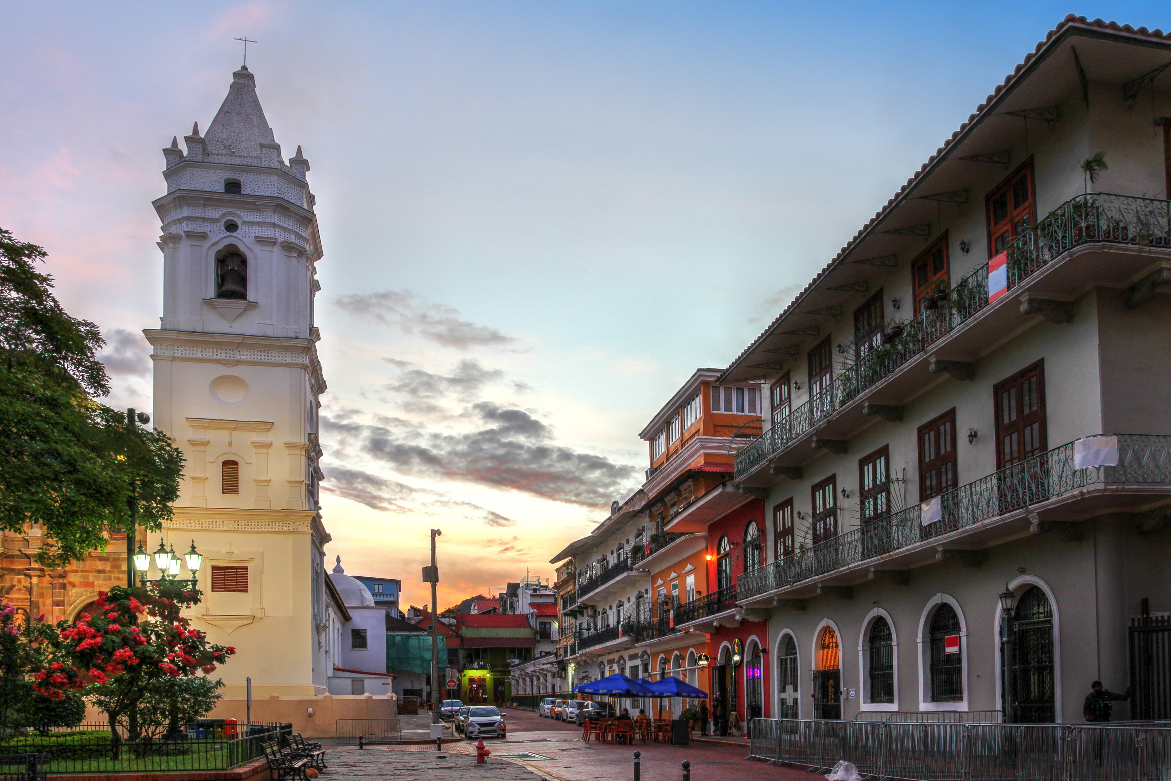 White church bell tower overlooks a vibrant street with colorful buildings at dusk.