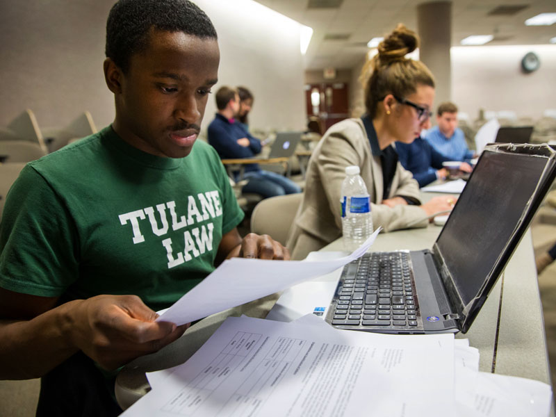 A student wearing a Tulane Law t-shirt looks at a paper in a classroom