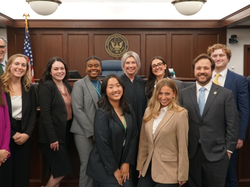 Law students pose for a photo with a judge in a courtroom.