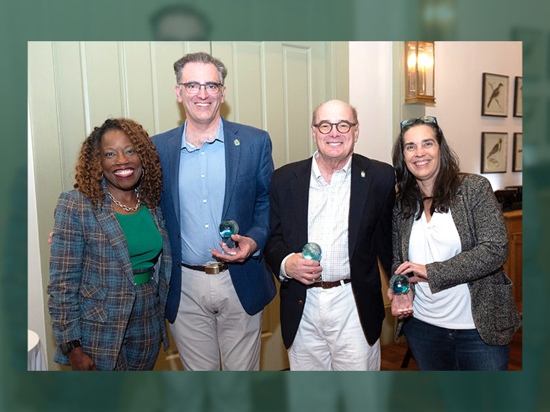 Four smiling people, two men and two women, holding transparent awards.