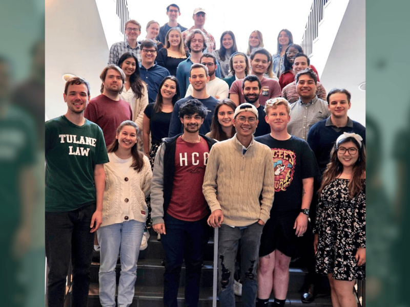 Diverse group of smiling people on a staircase, some wearing university t-shirts.
