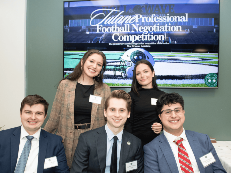Students pose for a photo in front of a sign that reads "Tulane Professional Football Negotiation Competition"