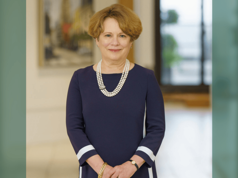 Smiling woman with reddish hair in a blue dress and pearl necklace.