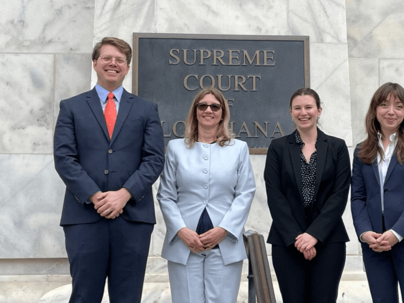 Four professionals stand smiling outside the Supreme Court building.