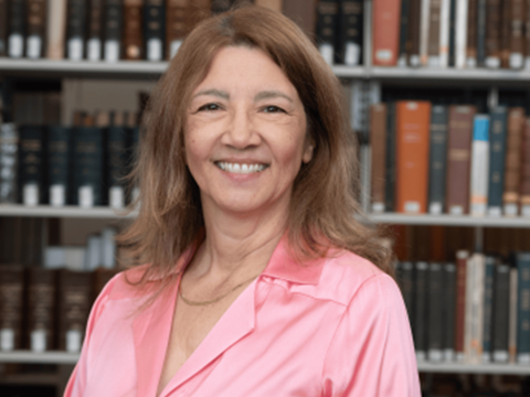 Photograph: Smiling woman in pink shirt, in front of blurred library bookshelves.