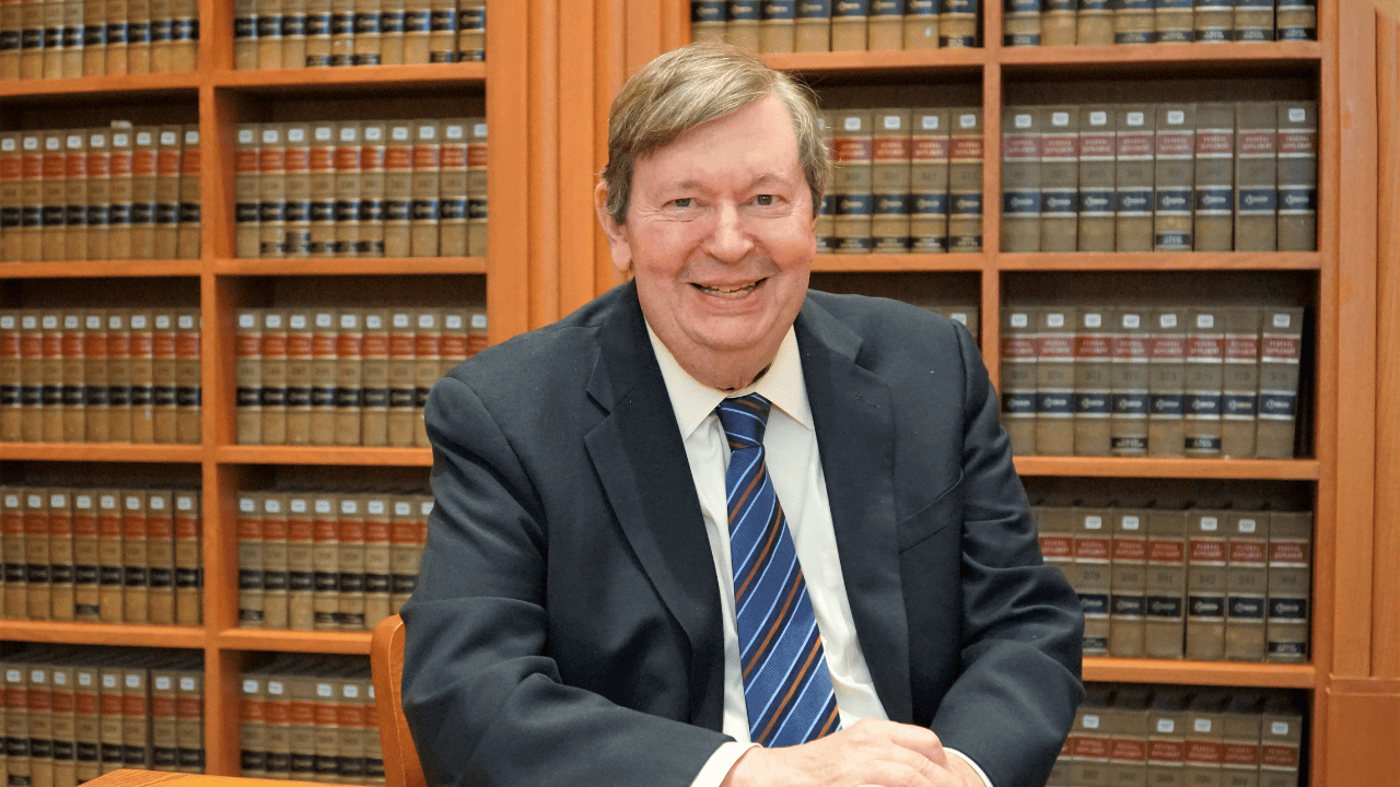 Professor Gordley smiles for a photo in front of stacks of books in a library.