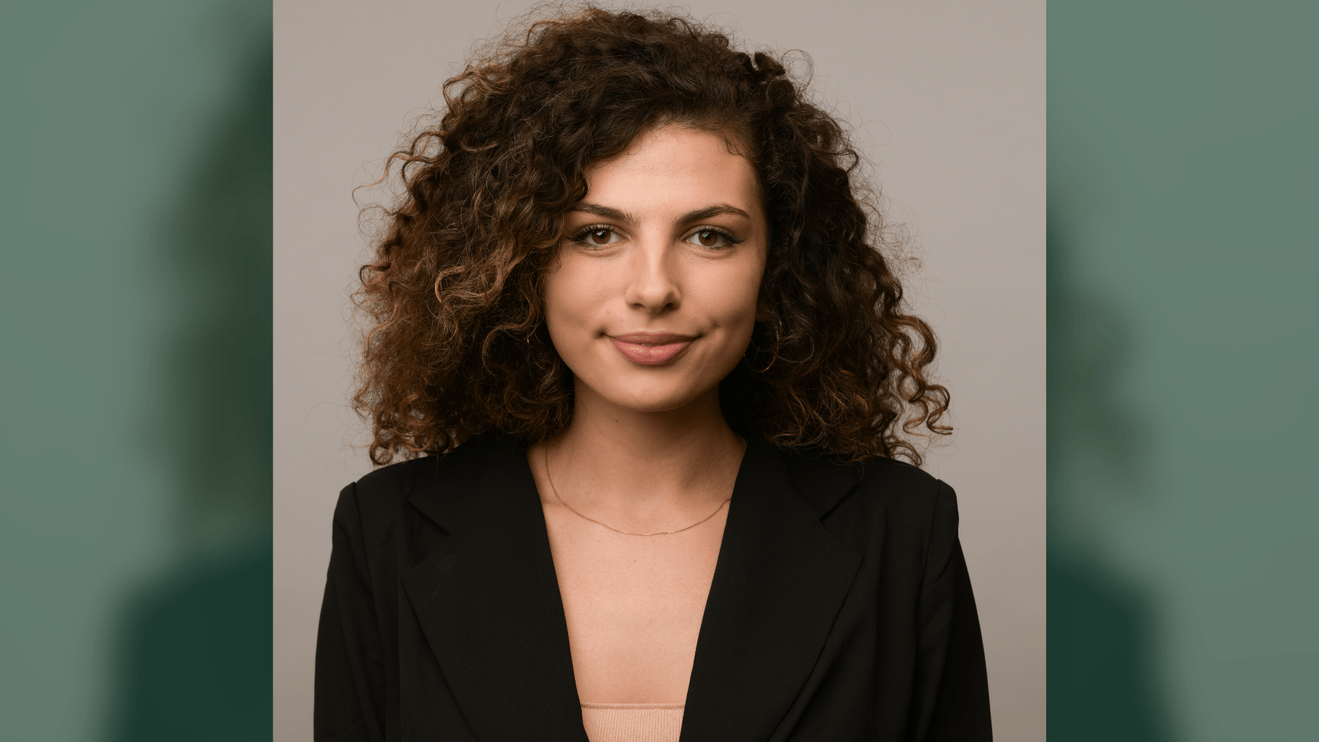 Professional photograph of a woman with curly brown hair, subtle smile, wearing a black blazer.