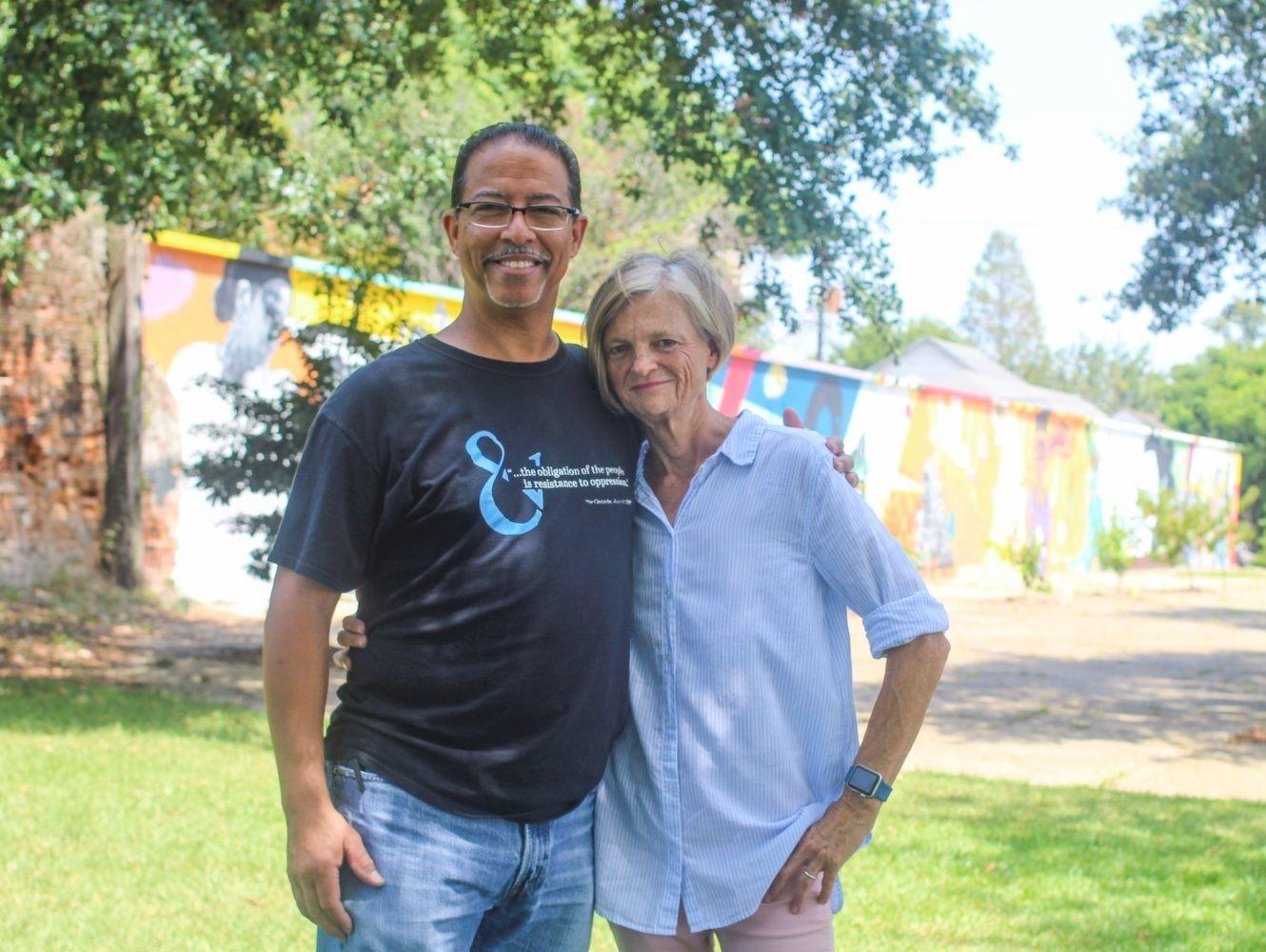Man in "resistance to oppression" shirt with woman, arm around her, smiling in front of a colorful mural.