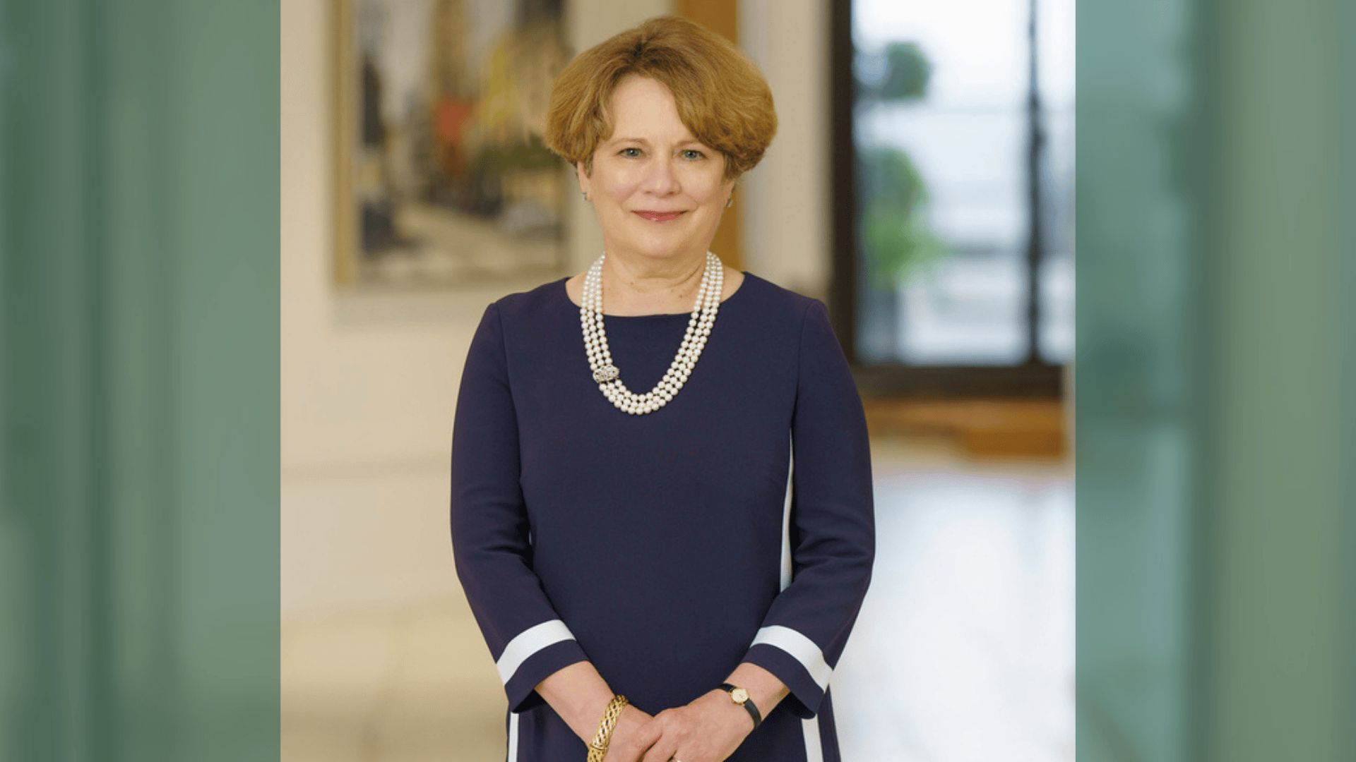 Smiling woman with reddish hair in a blue dress and pearl necklace.
