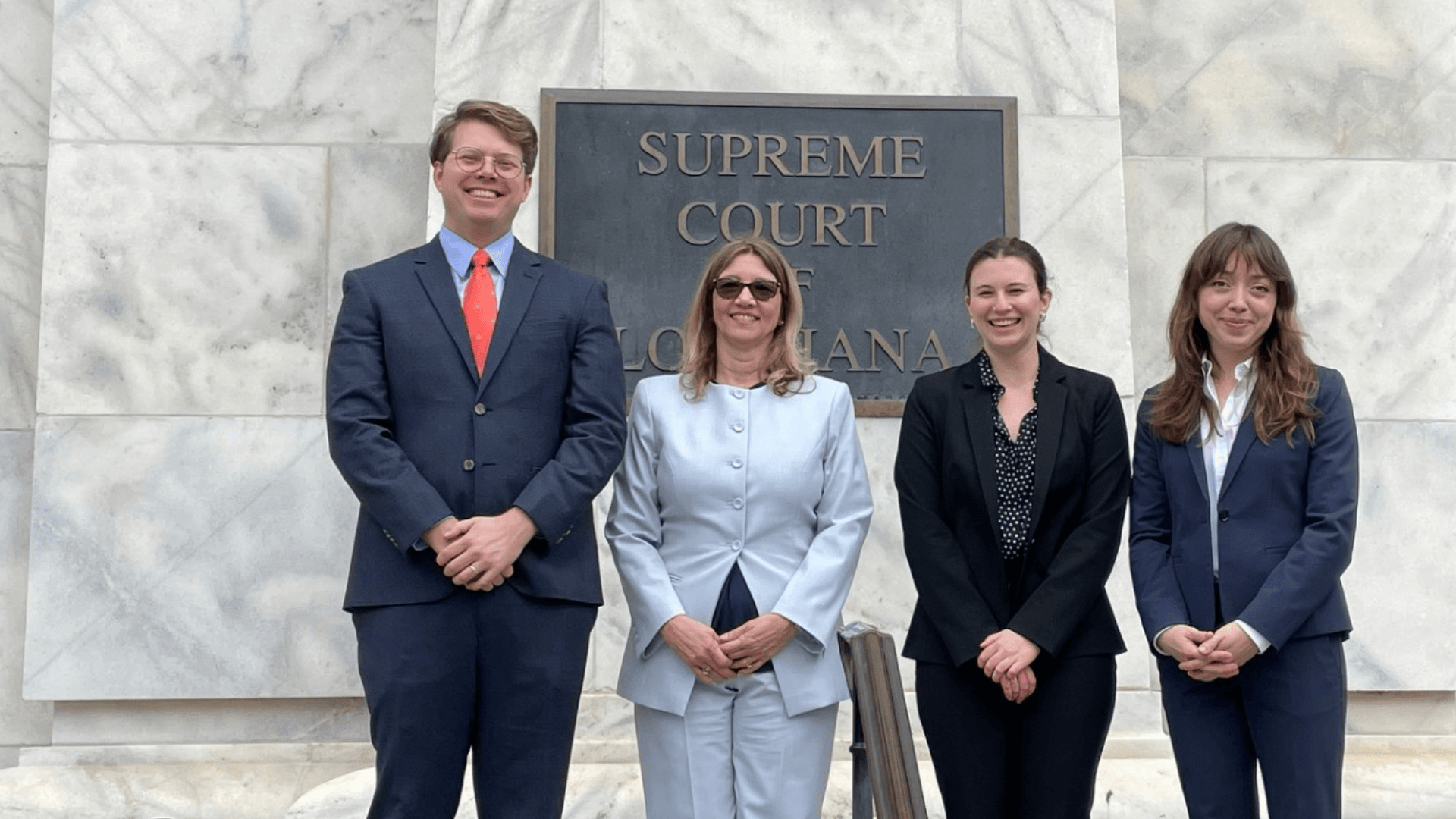Four professionals stand smiling outside the Supreme Court building.