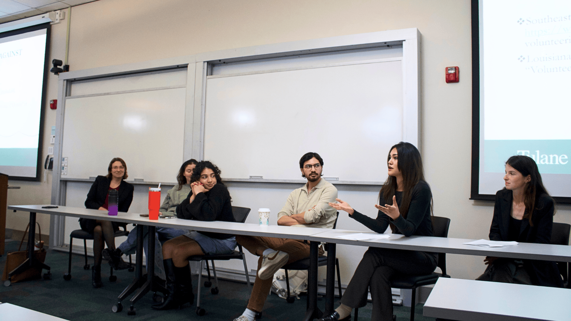 Five panelists sit at a table in a classroom, one woman actively speaks.