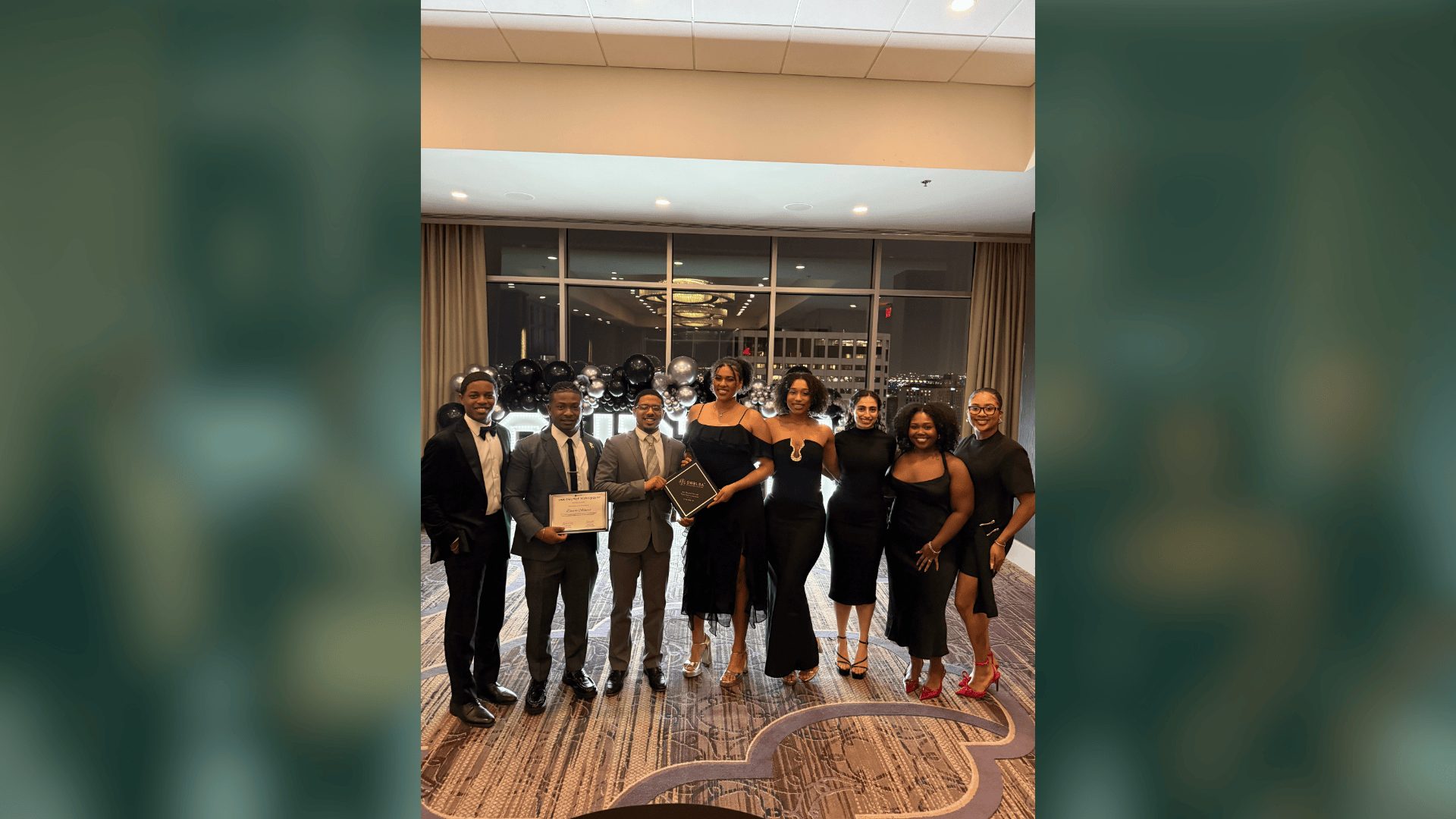 Eight people in formal wear, holding an award, at a celebratory event.