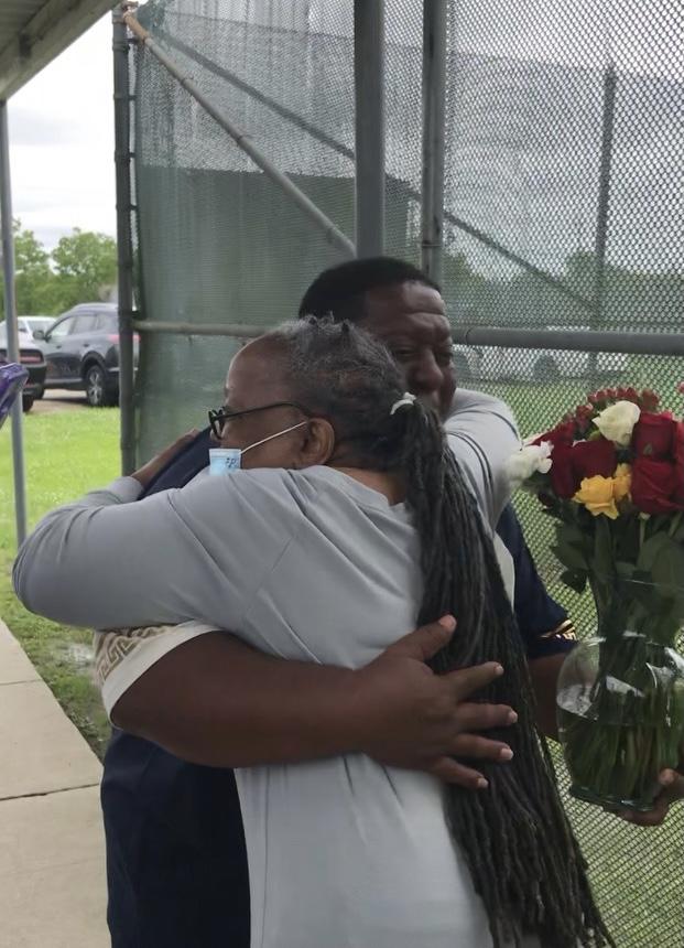 Mother and son embrace while son holds a vase of flowers