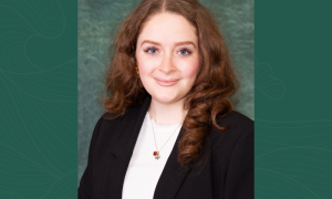 Laura Derbonne smiles for a headshot wearing a white blouse and black blazer. Laura's photo is set against a green background.