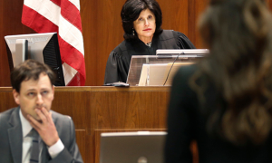 Sarah Vance sits in a courtroom, listening to another individual speak.