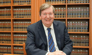 Professor Gordley smiles for a photo in front of stacks of books in a library.