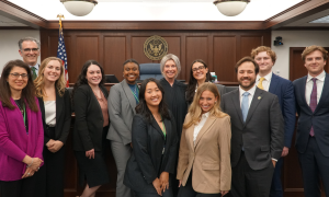 Law students pose for a photo with a judge in a courtroom.