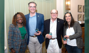 Four smiling people, two men and two women, holding transparent awards.