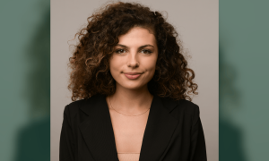 Professional photograph of a woman with curly brown hair, subtle smile, wearing a black blazer.