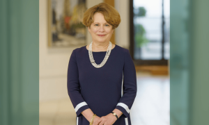 Smiling woman with reddish hair in a blue dress and pearl necklace.