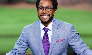 Desmond Howard in light blue suit, purple tie, and glasses, golf course background.