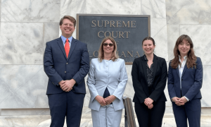 Four professionals stand smiling outside the Supreme Court building.